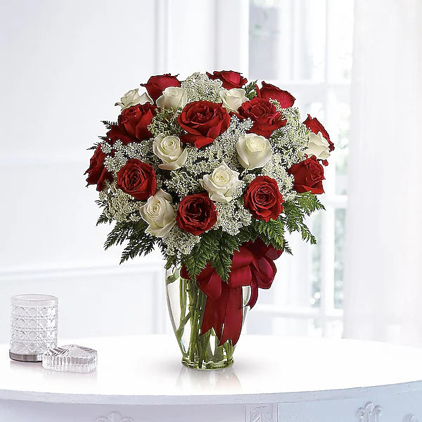 Bouquet of red and white roses in a clear vase with a red bow on a white surface.