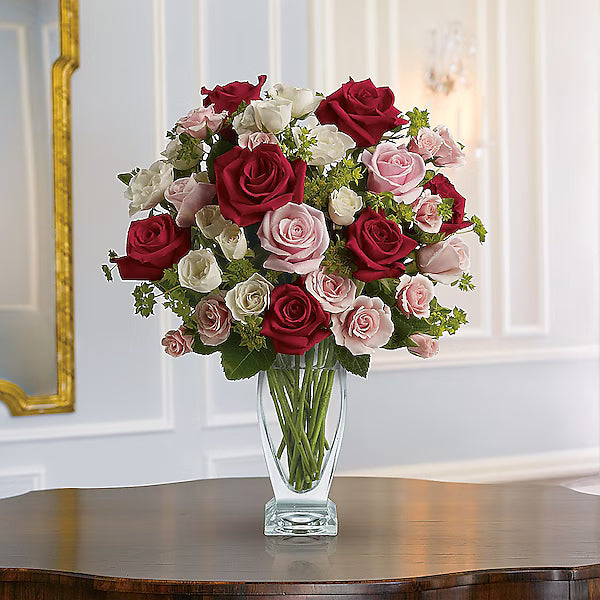 Red, white, and pink roses arranged in vase on tabletop.