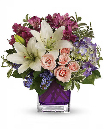White lilies, pink roses, and purple hydrangeas in a purple vase.